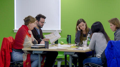 Five graduate students seated at a table with papers, snacks and drinks. One student is speaking.
