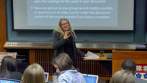 Medium wide shot of Professor Grotzer in front of the classroom explaining something to students.
