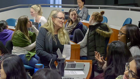 Professor Grotzer joining in on small group discussion. Graduate students in foreground and background engaged in discussion.