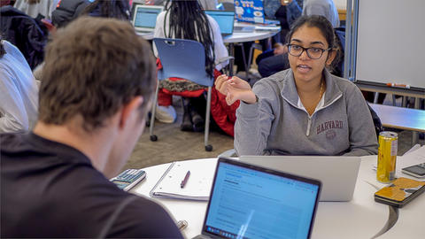 Close up of two students in front of computers at a small round table discussing